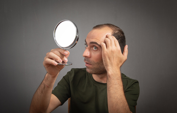 Bild zeigt Mann der sich im Spiegel begutachtet